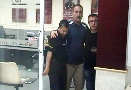 A rather dazed Kelek Veoat, center, is helped out of Pattaya Police Station after reporting the theft incident to officers on duty.